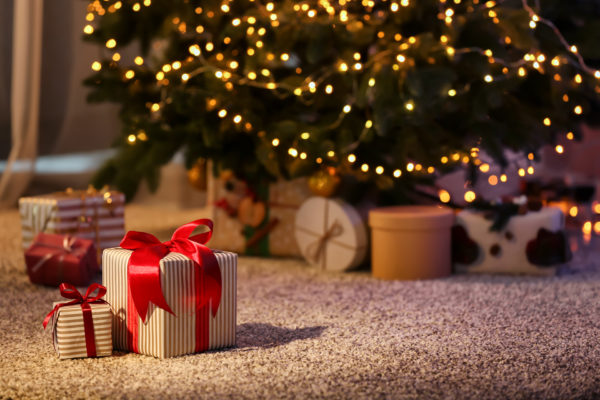 small present boxes wrapped with red ribbon and a bow on the top underneath a christmas tree which looks to be in a family home